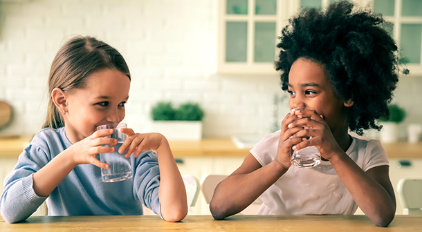 : Dos niñas compartiendo secretos y tomando agua. 
